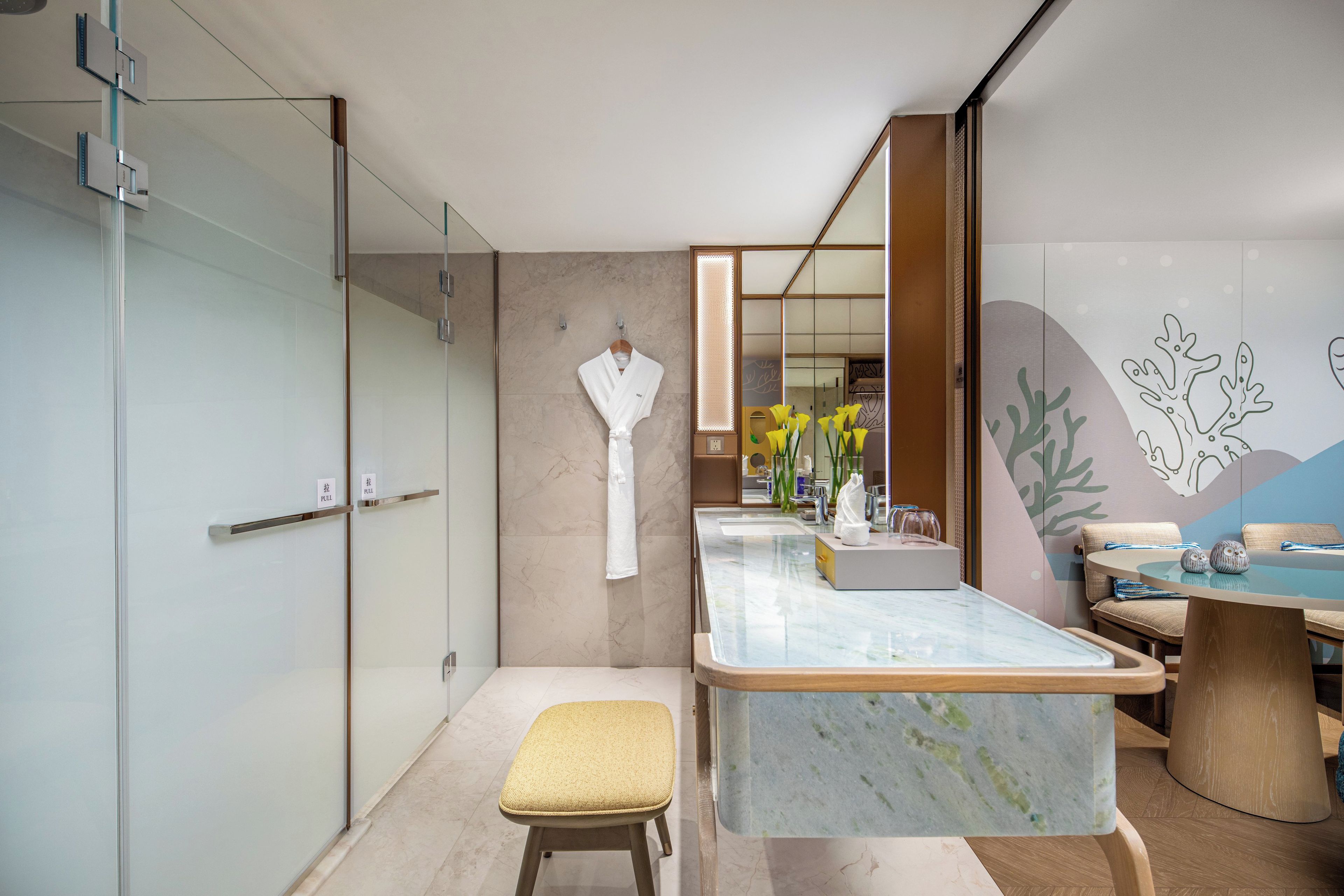 Une salle de bain moderne dotée d’une douche à parois de verre, d’un meuble-lavabo en marbre et d’un coin salon avec un banc.