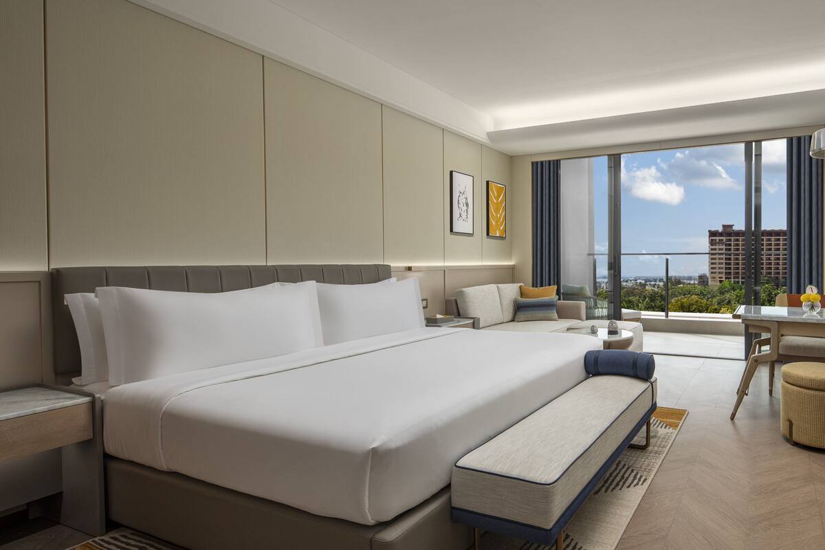 Une chambre d’hôtel moderne, dotée d’un grand lit, d’un petit canapé, d’un bureau et offrant une vue sur la ville.