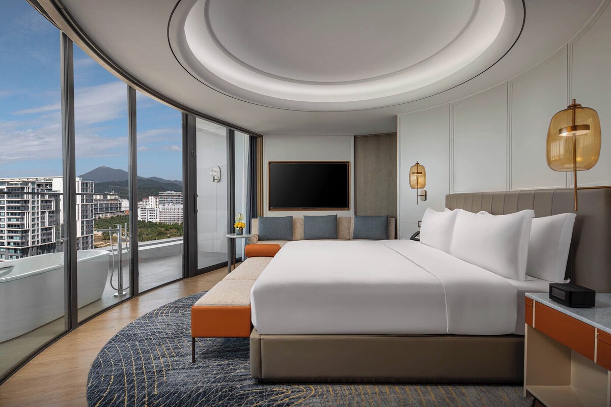 Een moderne hotelkamer met een groot bed, een televisie, een balkon met uitzicht op de stad en een rond dakontwerp.