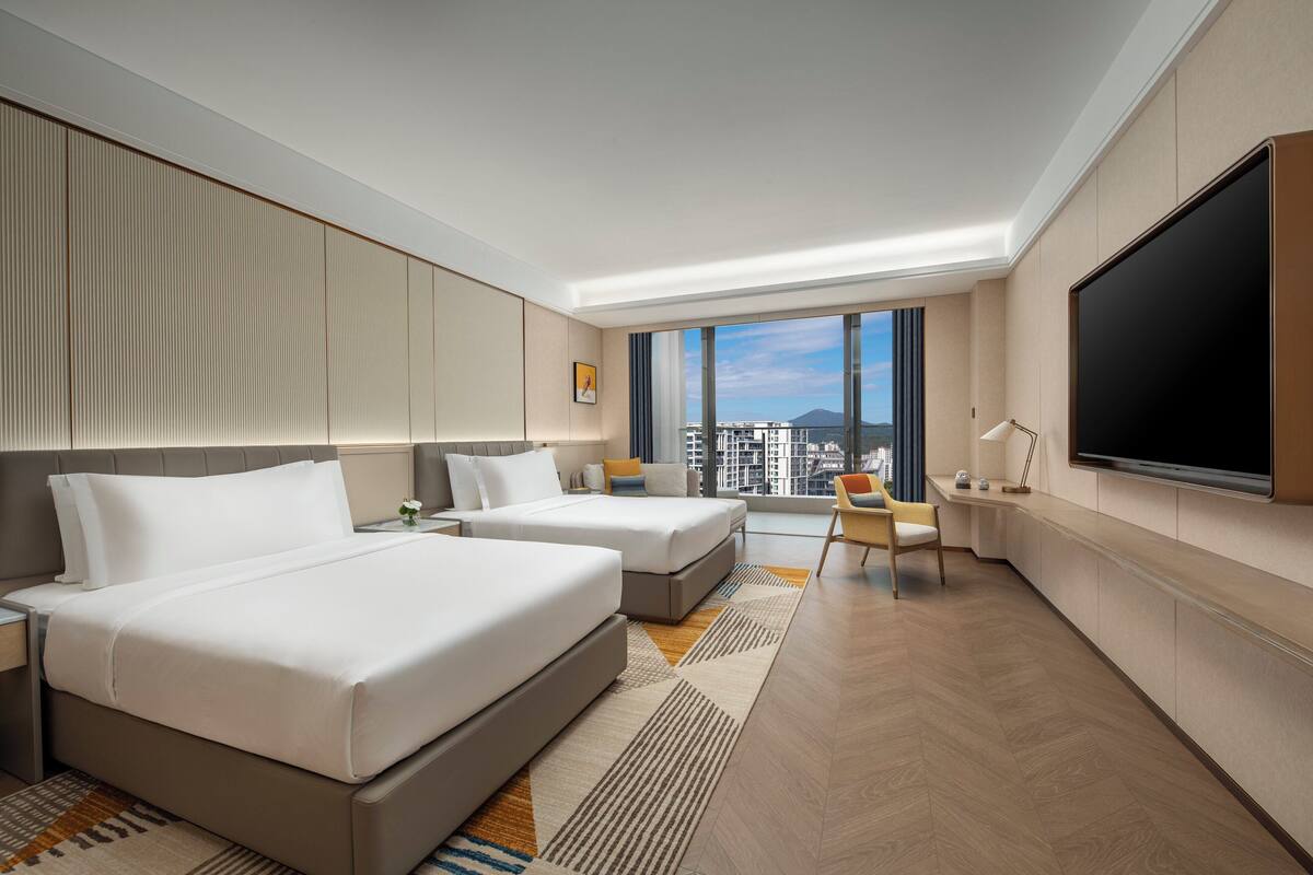 Une chambre d’hôtel moderne dotée de deux lits, d’un téléviseur à écran plat, d’un bureau et d’une grande fenêtre donnant sur la ville.