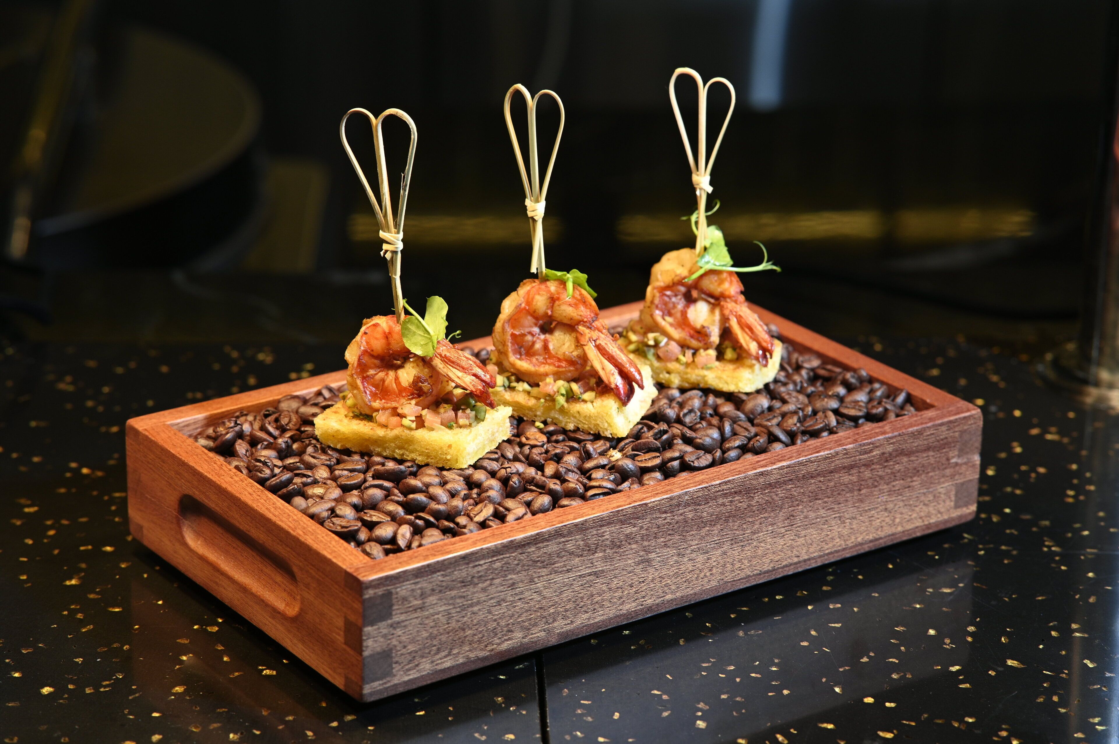 Three appetizers on a wooden tray with coffee beans.