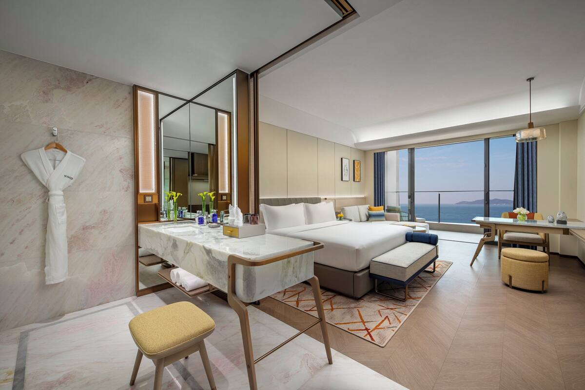 Une chambre d’hôtel moderne dotée d’un grand lit, d’un bureau, d’un coin salon et offrant une vue sur l’océan.