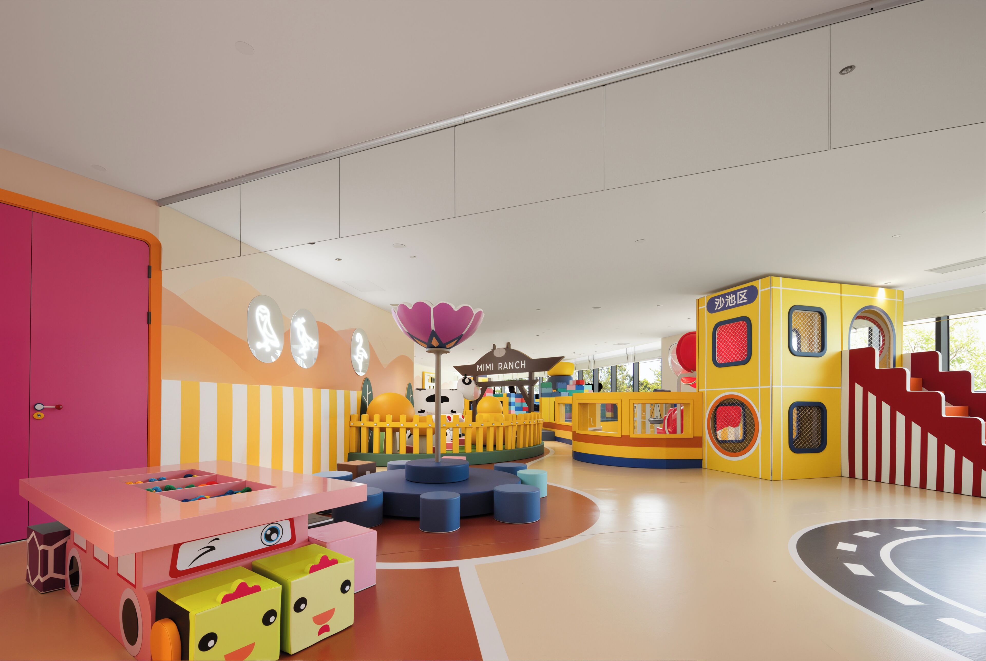 Ein Kinderspielbereich mit bunten Spielgeräten, einem rosafarbenen Tisch und einem gelben Spielhaus.