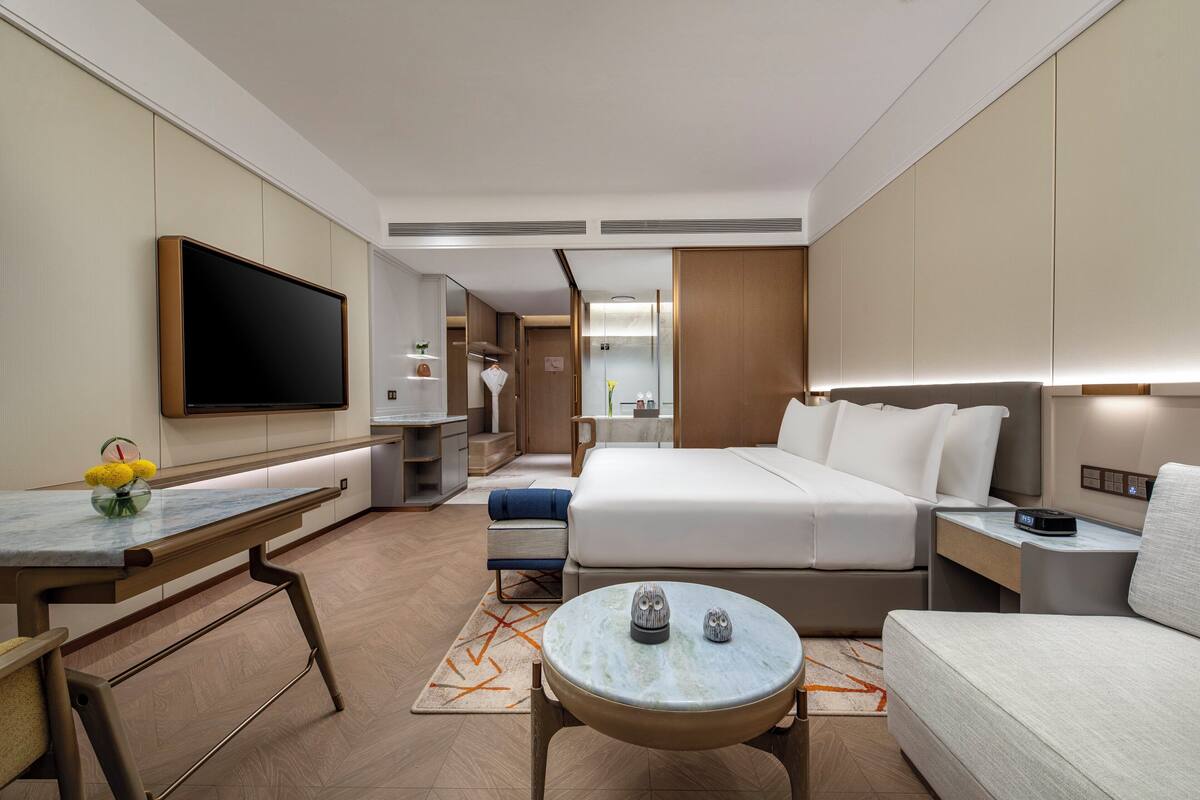 Una habitación de hotel moderna con una cama grande, un televisor de pantalla plana, un escritorio y una pequeña mesa redonda con adornos.