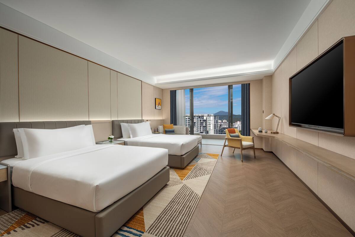 Une chambre d’hôtel moderne avec deux lits, une grande télévision et une vue sur la ville.