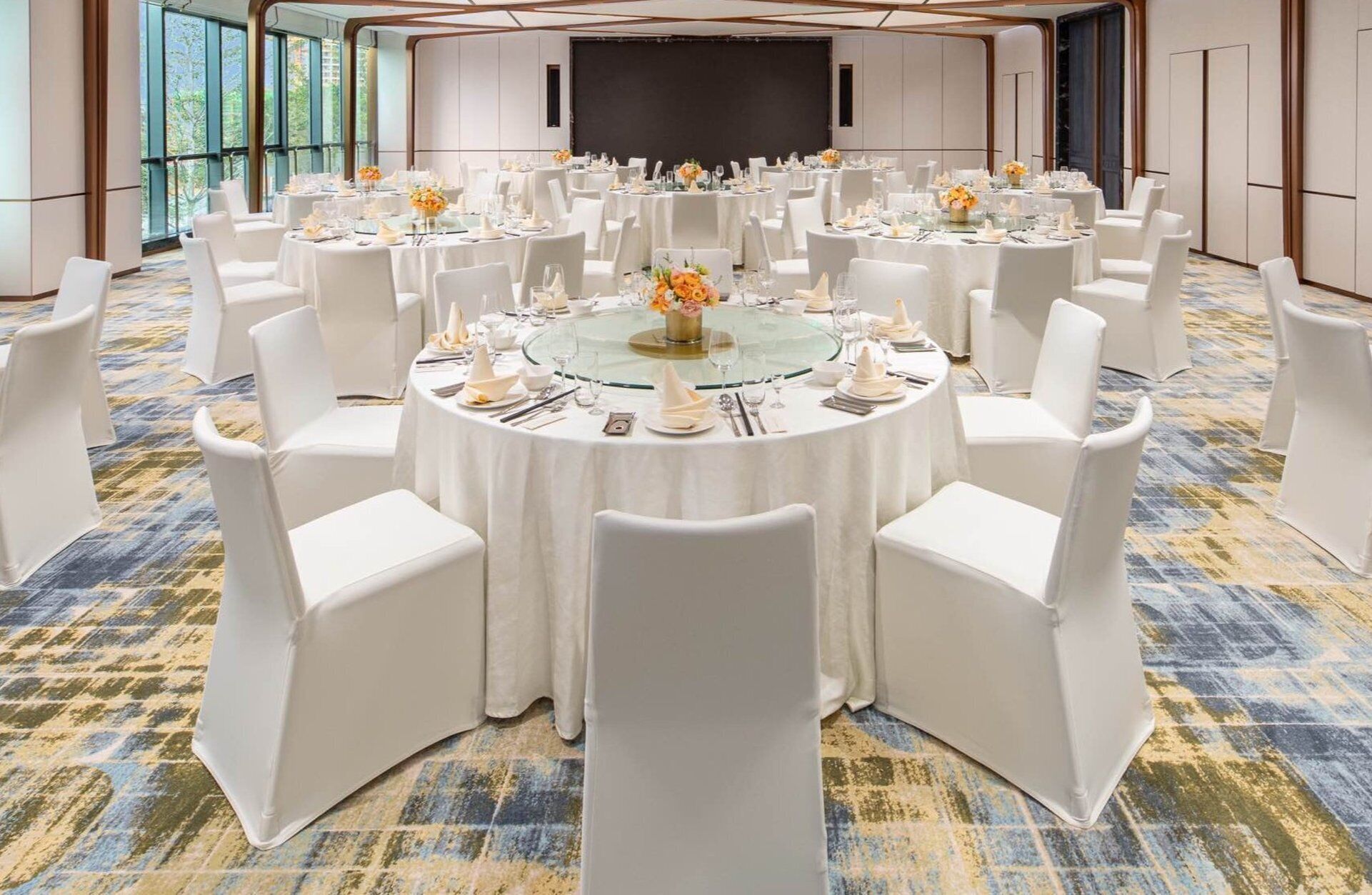 Une salle de conférence avec des tables rondes, des chaises blanches et un grand écran.