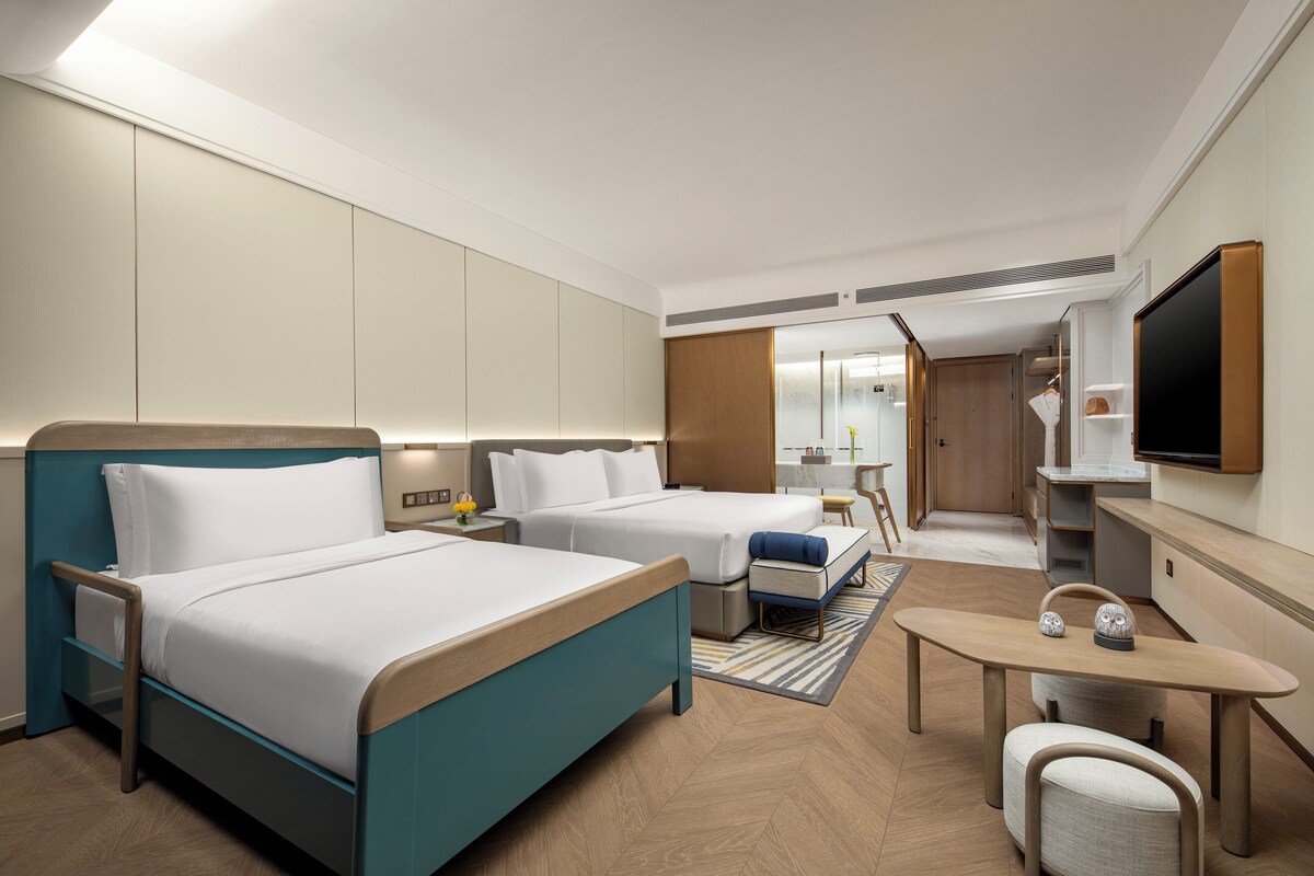 Een hotelkamer met twee bedden, een bureau, een stoel, een televisie en een badkamer die door een open deur zichtbaar is.