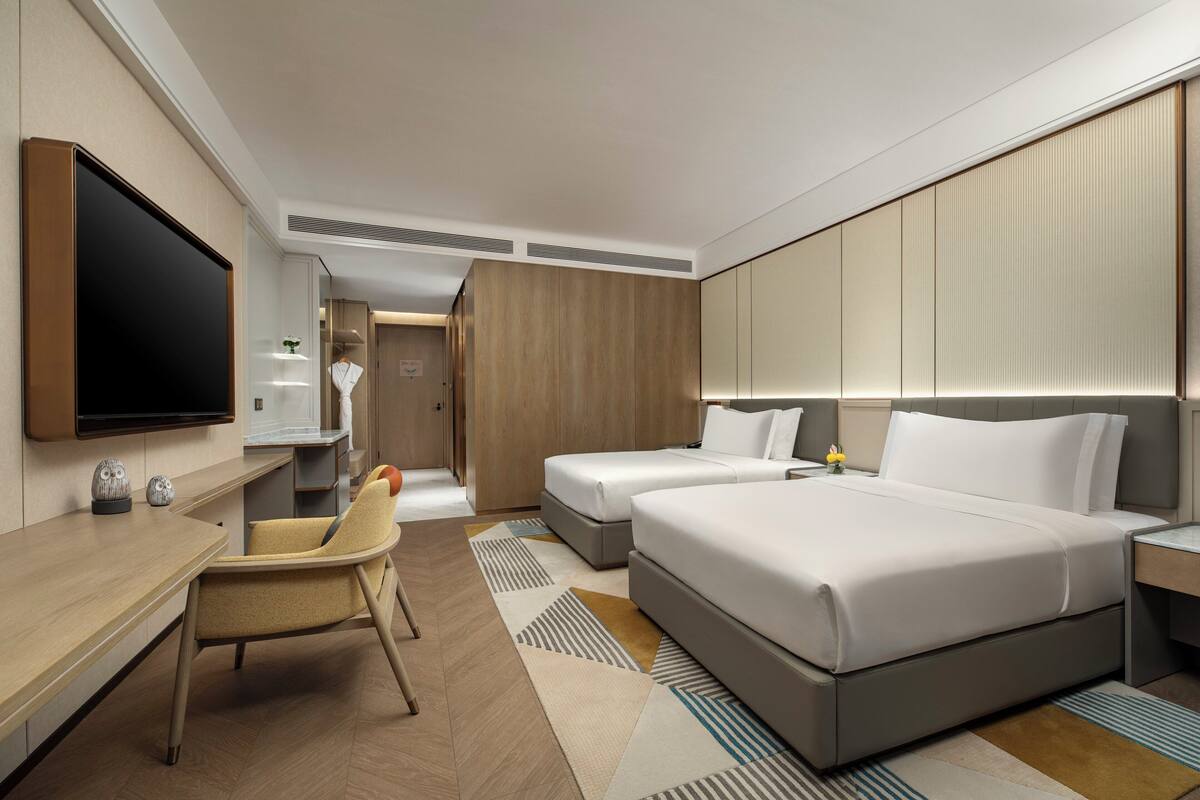 Una habitación de hotel moderna con una televisión de pantalla plana, un escritorio, dos camas y una silla.