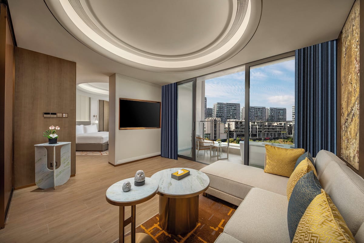 A modern hotel room with a balcony, a sofa, a TV, and a small table with decorative items.