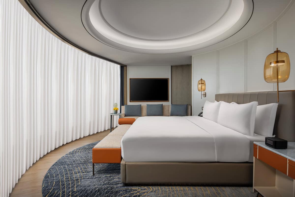 A modern hotel room with a large bed, a bedside table, a flat-screen TV, and a round rug.