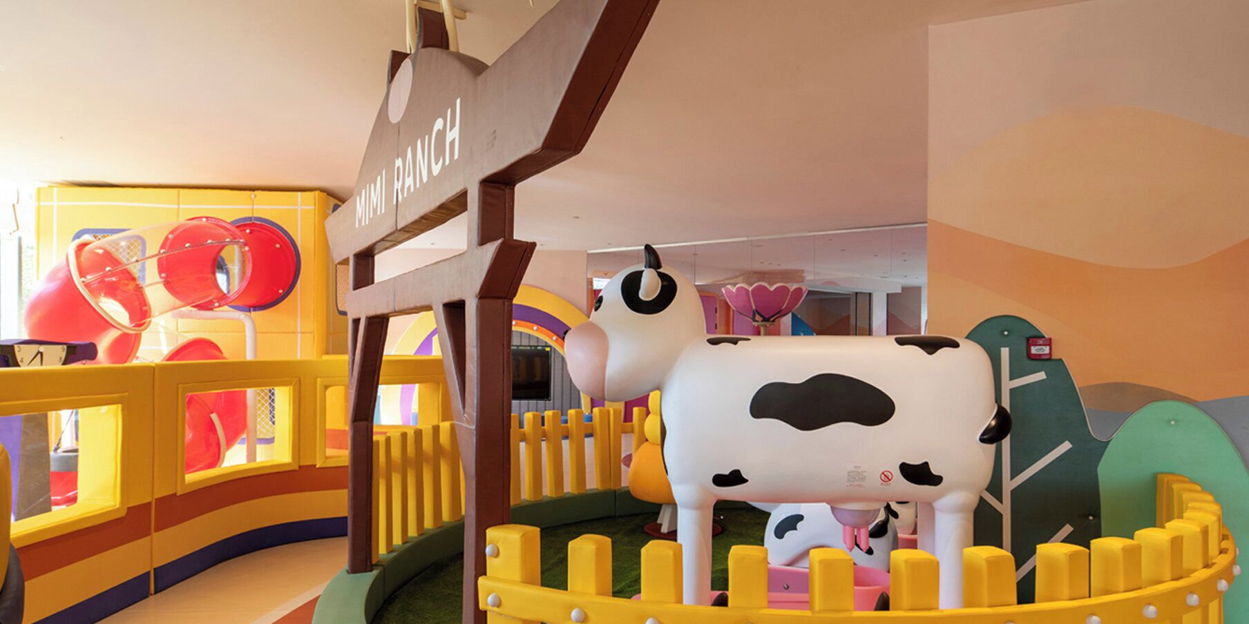 Un espace de jeux pour enfants avec une structure ludique en forme de vache et une pancarte indiquant « Mimi Ranch ».