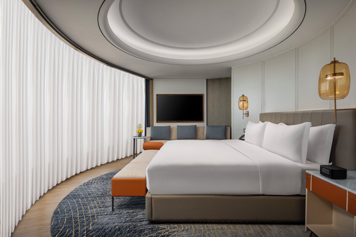 Una habitación de hotel moderna con una cama grande, una mesita de noche, un televisor de pantalla plana y una alfombra redonda.