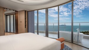 Une chambre d’hôtel moderne dotée d’un grand lit, offrant une vue sur la mer et comprenant un balcon avec une baignoire.
