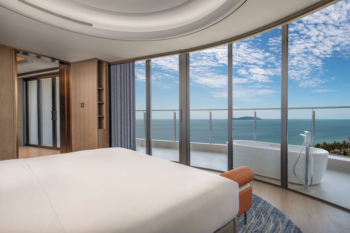 Une chambre d’hôtel moderne dotée d’un grand lit, offrant une vue sur la mer et comprenant un balcon avec une baignoire.