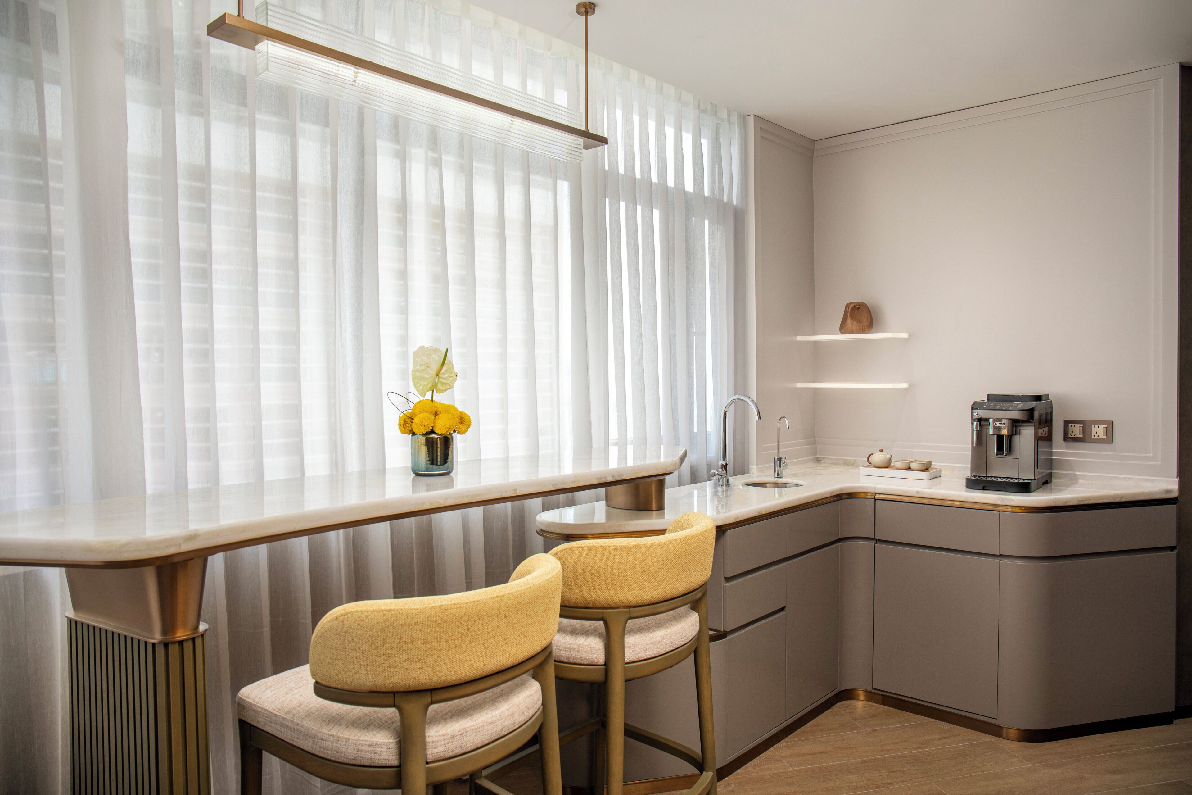 Een moderne keuken met een bar, voorzien van een marmeren aanrechtblad, twee barkrukken, een koffieapparaat en een vaas met bloemen.
