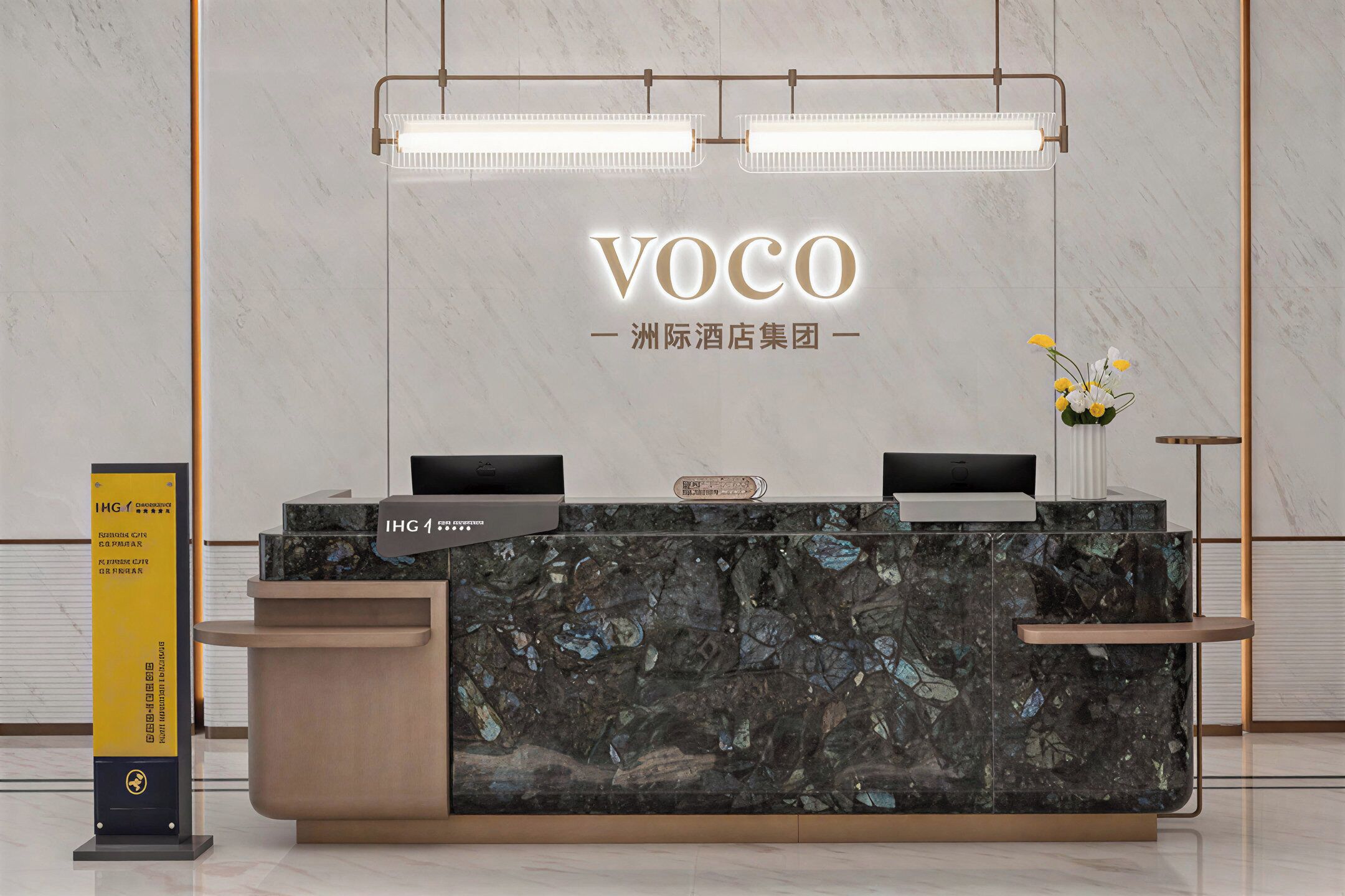 A reception desk with a marble top, two monitors, and a sign indicating IHG membership.
