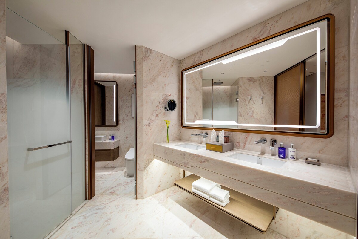 Un baño moderno con un espejo grande, dos lavamanos, un inodoro y una zona de ducha.