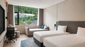 Une chambre d’hôtel avec deux lits, un bureau, une chaise, une télévision et une fenêtre donnant sur un paysage verdoyant.