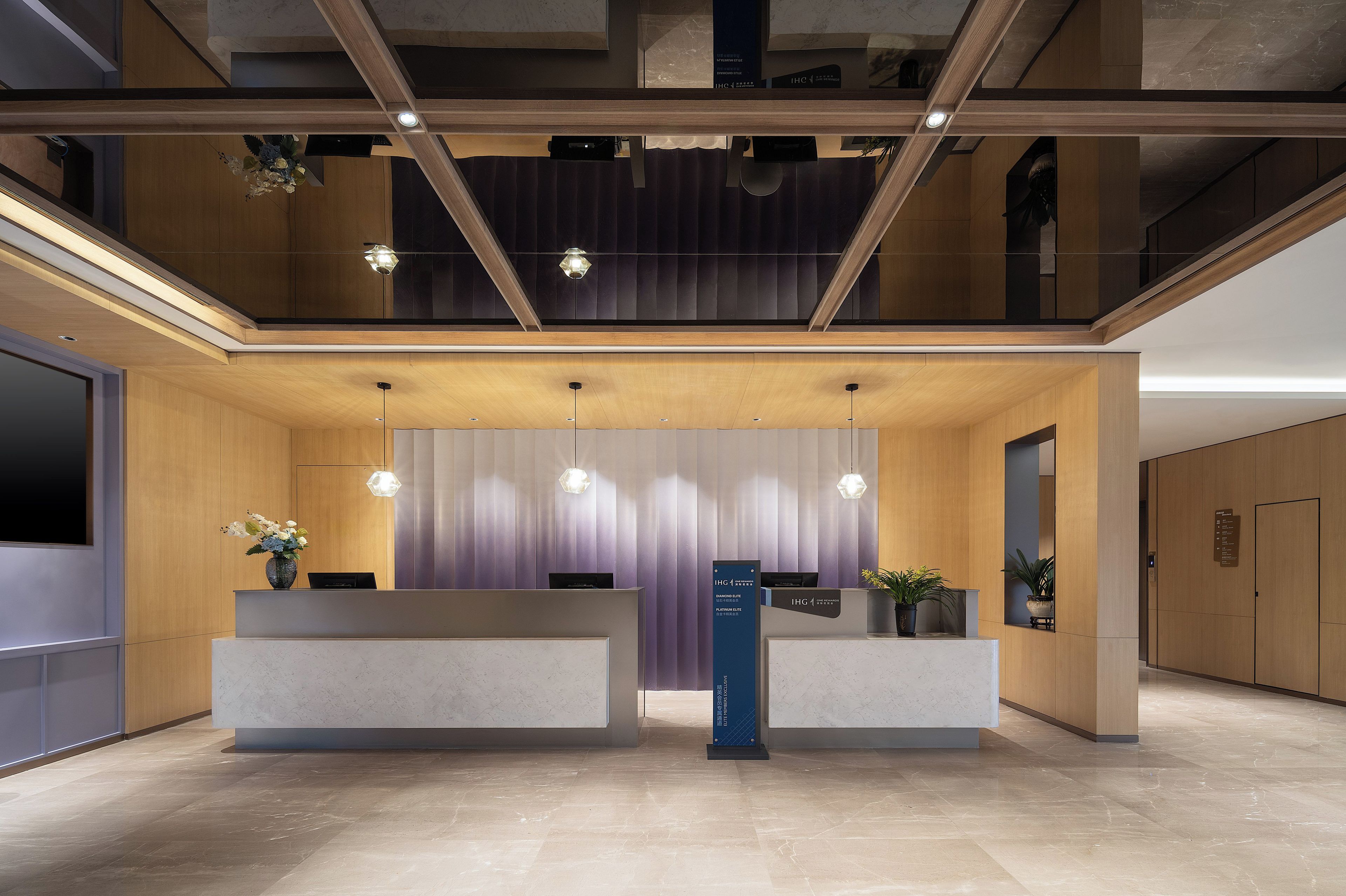 A modern reception area with a wooden reception desk, a vertical sign, and a ceiling with exposed beams and pendant lighting.