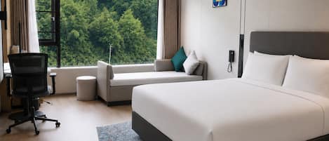 Habitación de hotel moderna con una cama grande, un sofá, un escritorio y vistas a zonas verdes por la ventana.