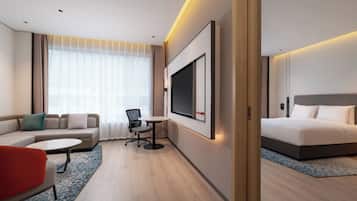 A modern hotel room with a sofa, a small table, a desk, a bed, and a TV.