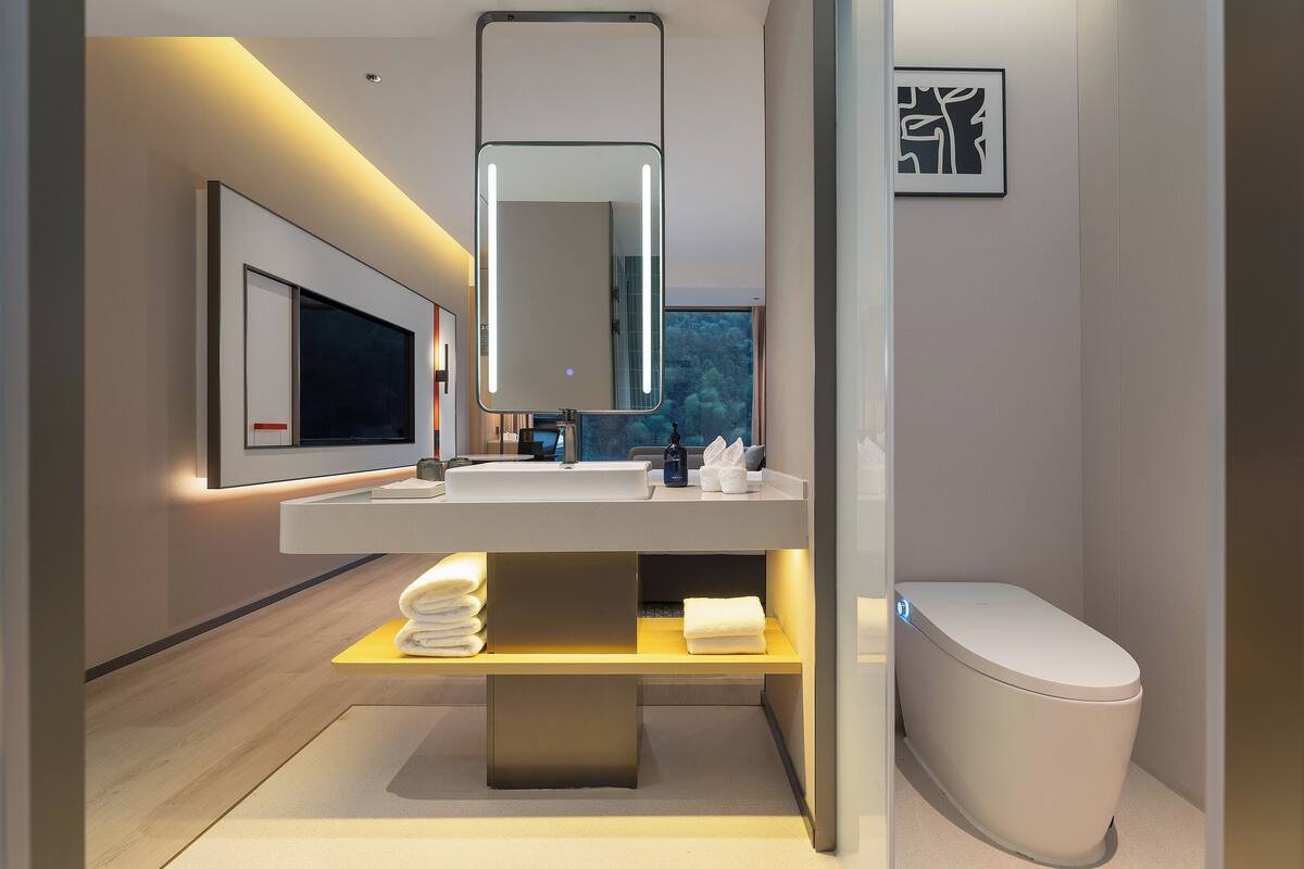 A modern bathroom with a large mirror, a sink, a toilet, and a towel rack.