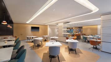A modern dining area with tables and chairs, a kitchen in the background, and a curved ceiling design.