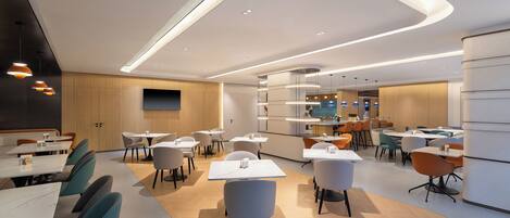 A modern dining area with tables and chairs, a kitchen in the background, and a curved ceiling design.