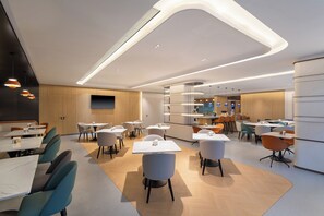 A modern dining area with tables and chairs, a kitchen in the background, and a curved ceiling design. - Holiday Inn Express Huangshan Mountain South Gate By Ihg (Huangshan)