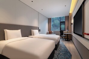 Hotellihuone, jossa on kaksi sänkyä, työpöytä, tuoli ja suuri ikkuna.