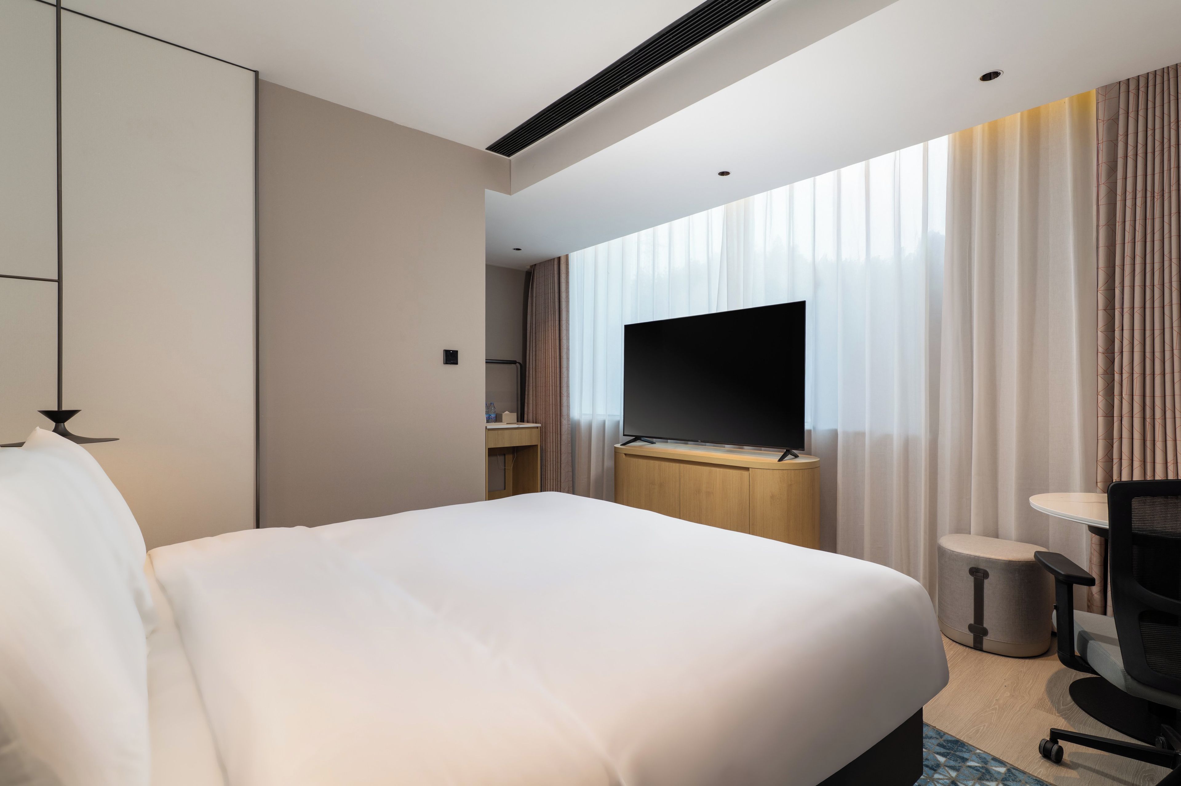 A modern hotel room with a large bed, a flat-screen TV, a desk, and a chair.