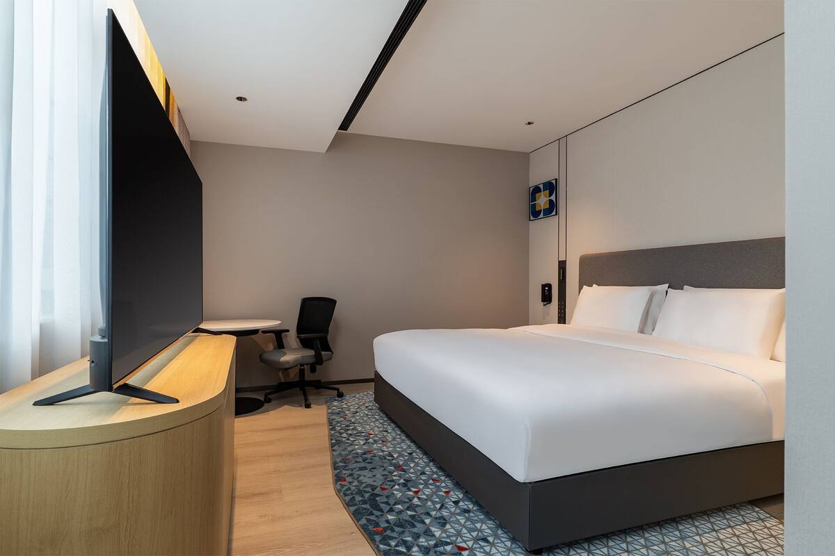 A hotel room with a bed, a desk, a chair, and a TV.