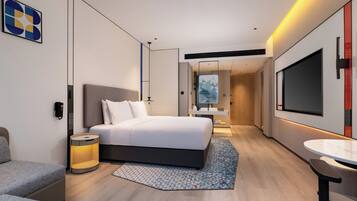 A modern hotel room with a large bed, bedside table, lamp, and a TV on the wall.