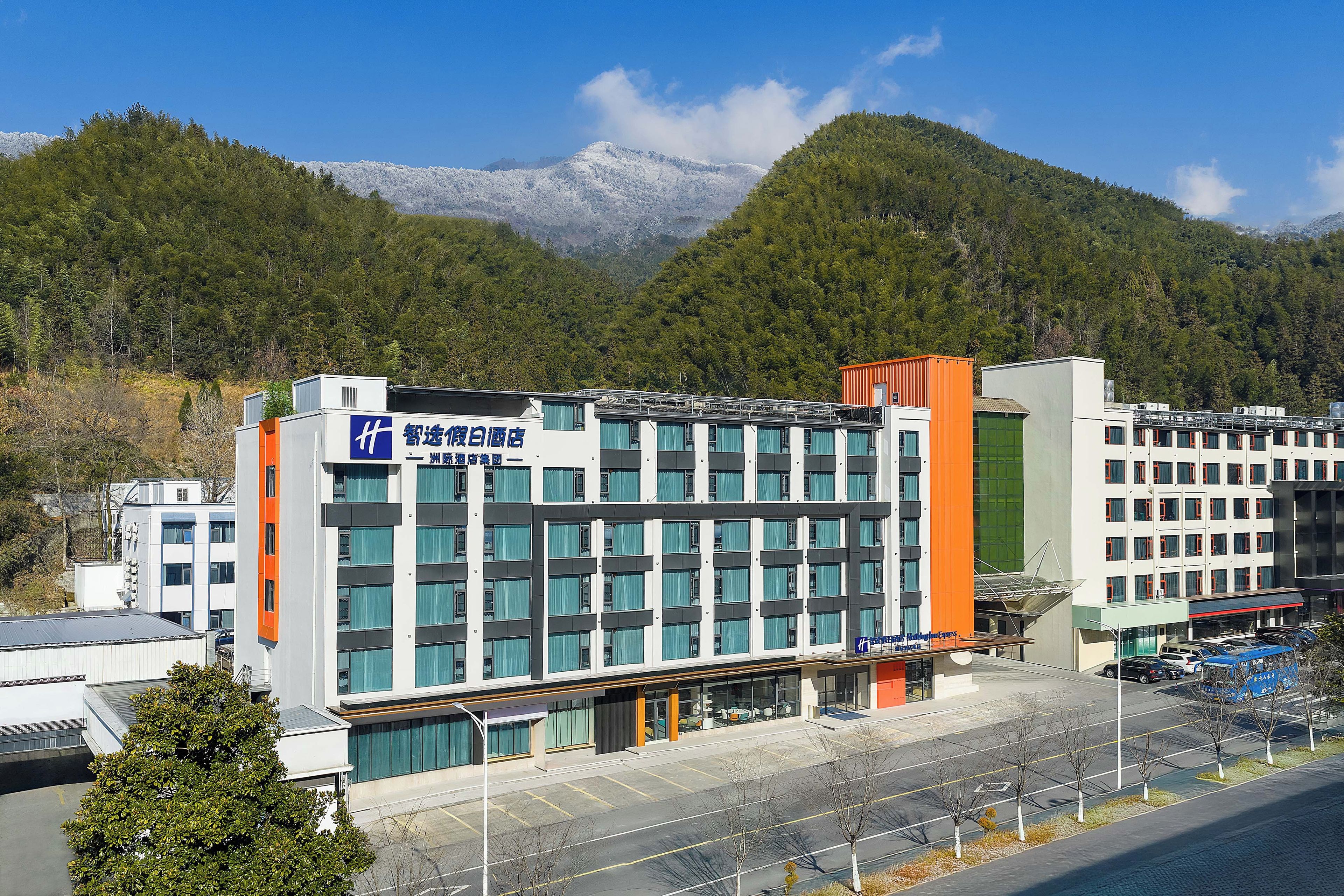 Un edificio moderno con varios pisos, ventanas amplias y un estacionamiento al frente.