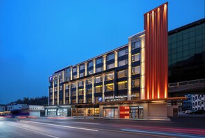 A modern hotel with a prominent vertical orange accent, multiple floors, and a well-lit facade. - Holiday Inn Express Huangshan Mountain South Gate By Ihg (Huangshan)