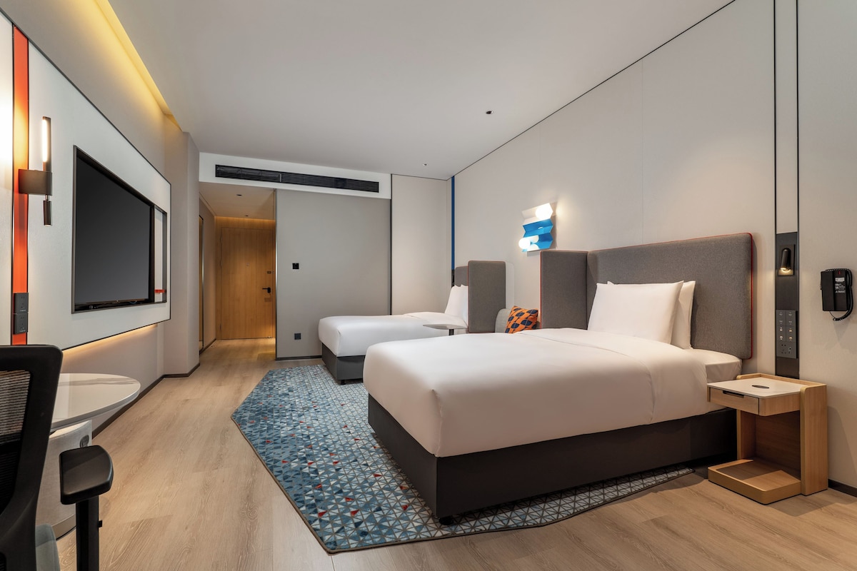 A modern hotel room with a large bed, a desk, a TV, and a small seating area.