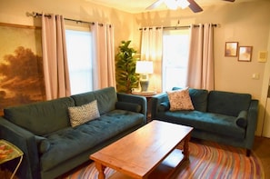 A living room with two green sofas, a wooden coffee table, a lamp, and a large window with curtains.