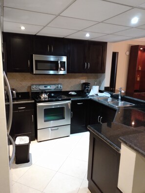 A modern kitchen with dark cabinetry, stainless steel appliances, and a tiled backsplash. - Lovely 2BR Presidential suite Hideaway: Your Air-Conditioned Tropical Paradise (Puerto Plata)