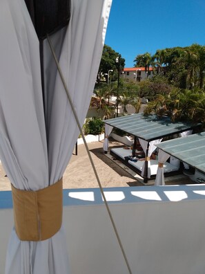 A beachside view with a white canopy structure, a sandy area, and a building with a red roof in the background. - Lovely 2BR Presidential suite Hideaway: Your Air-Conditioned Tropical Paradise (Puerto Plata)