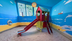 A play area with a slide, climbing structure, and a window with a view of trees. - Cottage with HotTub & Indoor Pool on Cornwall Farm (Searles) (Lostwithiel)
