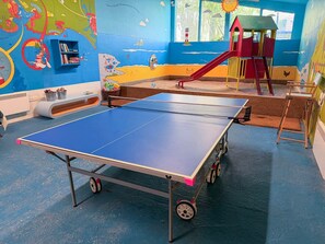 Ein Spielbereich für Kinder mit einer Tischtennisplatte, einer Rutsche und farbenfrohen Wandgemälden.