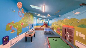 Ein Spielbereich für Kinder mit einer Tischfußballplatte, einem Billardtisch und einer Rutsche.