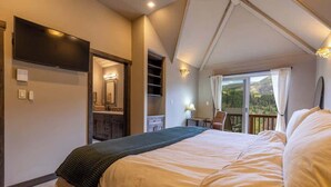 Un dormitorio con una cama grande, un televisor montado en la pared, un escritorio con una silla y un balcón con vistas al exterior.