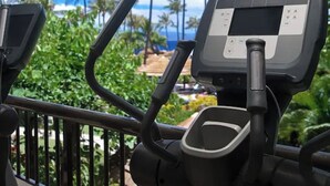 An exercise machine with a digital display, positioned in a room with a view of palm trees and a clear sky.