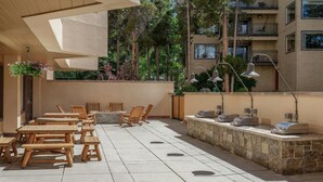 Un patio al aire libre con mesas y sillas de madera, un muro de piedra y una cesta de flores colgante.