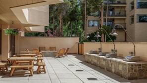 Eine Terrasse im Freien mit Holztischen und -stühlen, einer Steinsäule und einem hängenden Blumenkorb.