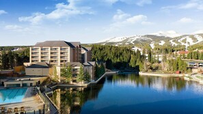 Um hotel com piscina, com montanhas ao fundo e um lago.