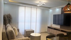Un salon moderne avec un canapé, un pouf et un téléviseur à écran plat fixé au mur.