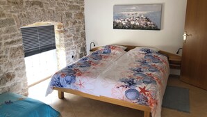 A bedroom with a stone wall, a bed with floral bedding, a painting of a town, and a window with blinds. - Istrian Family Villa Shopacita - family, bike & pet friendly<3 (Tar)