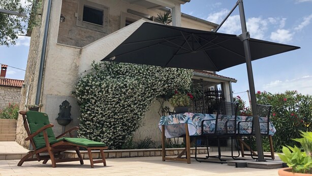 A building with a tiled roof, a large black umbrella, and a table with chairs. - Istrian Family Villa Shopacita - family, bike & pet friendly<3 (Tar)